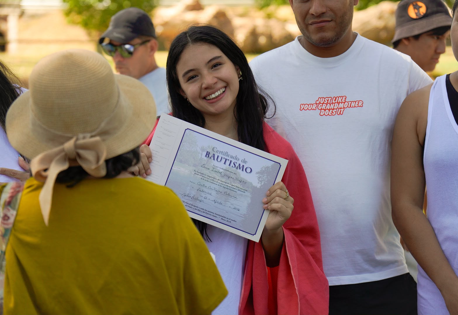 Una persona sonríe mostrando su certificado de bautismo
